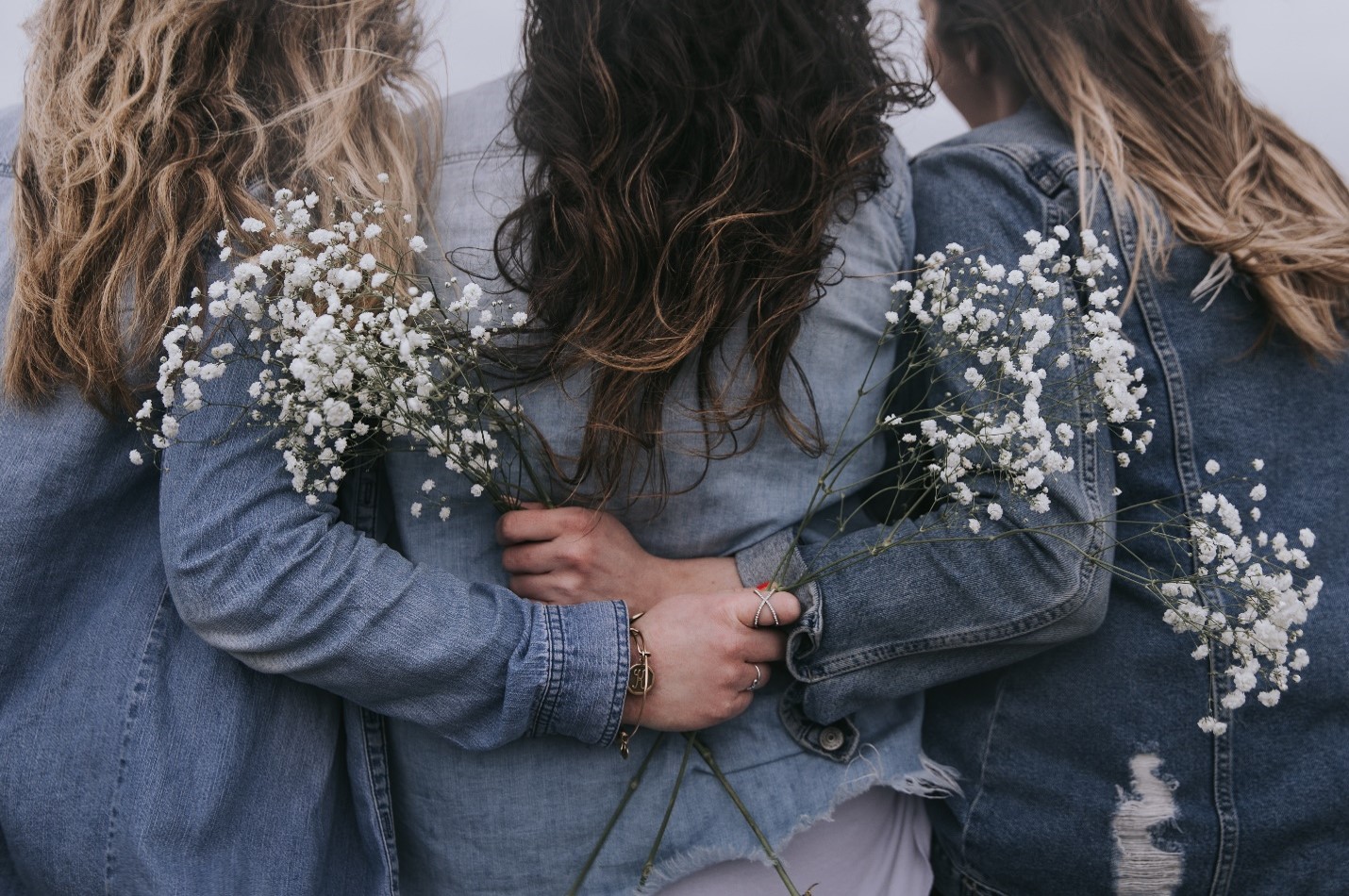 group of three girls holding flowers with arms around each other