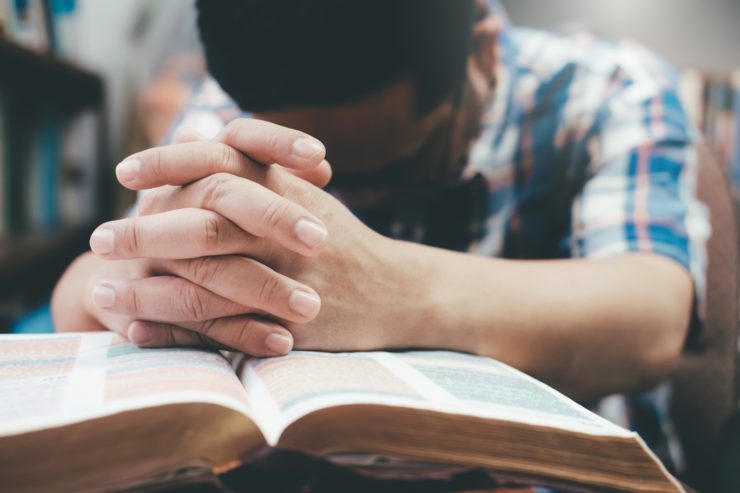 man praying with hands together on bible
