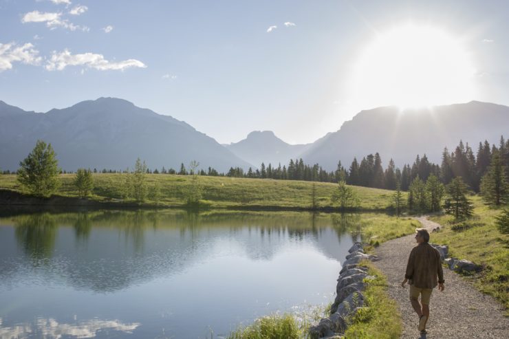 Man walks along pathway beside a lake towards the rising sun