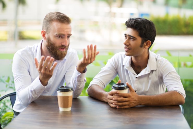 two men talking at table outside