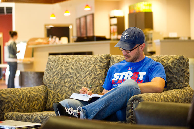 man sitting on couch and writing in book