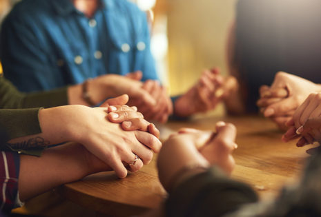 group of people holding hands around table