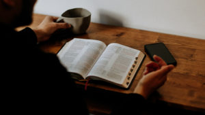 person with coffee cup phone and bible on table