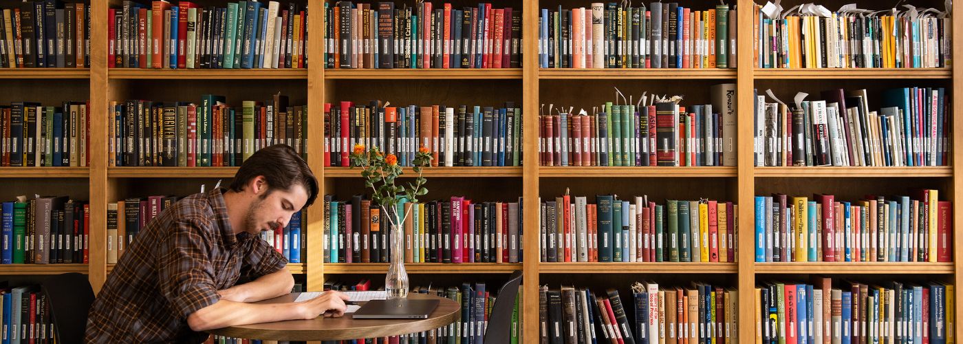 colorful stacks of books with student sitting at table in front