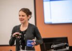 female professor standing in class holding coffee mug