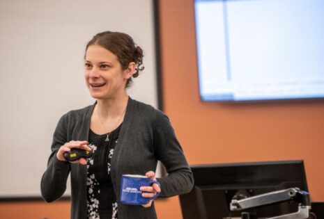 female professor standing in class holding coffee mug